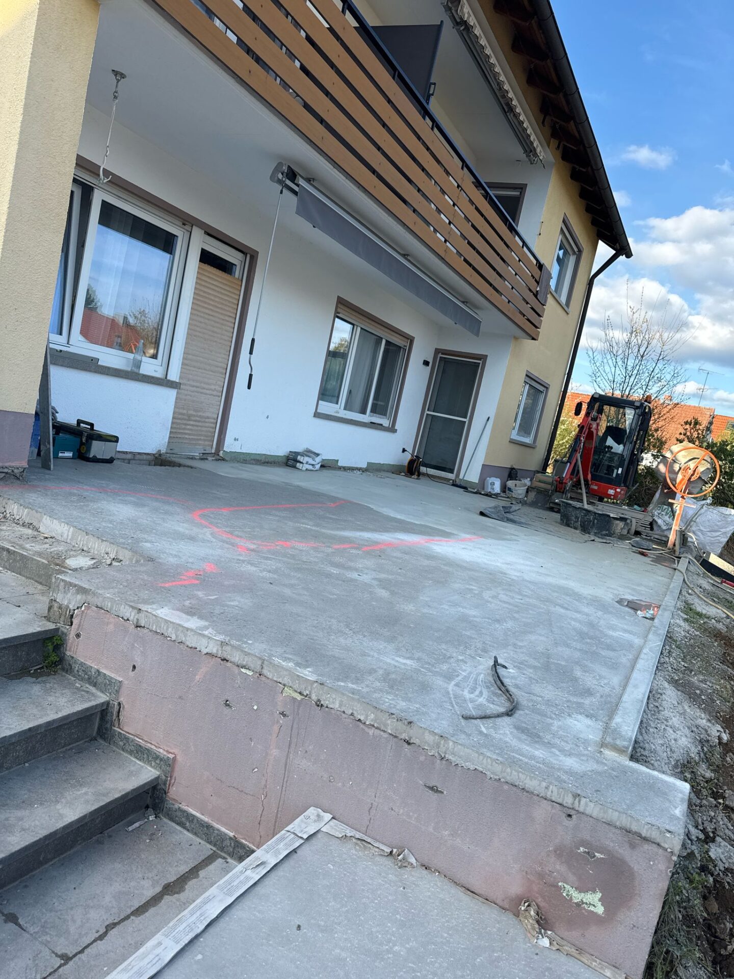 Hausfassade mit Baustelle, Terrasse und Mini-Bagger