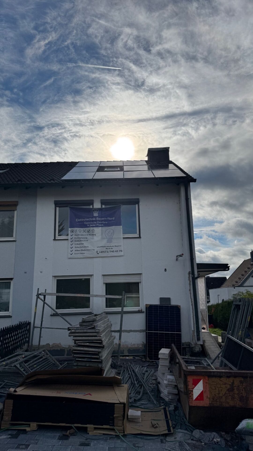 Haus mit Solarmodulen und Baugerüst bei bewölktem Himmel.