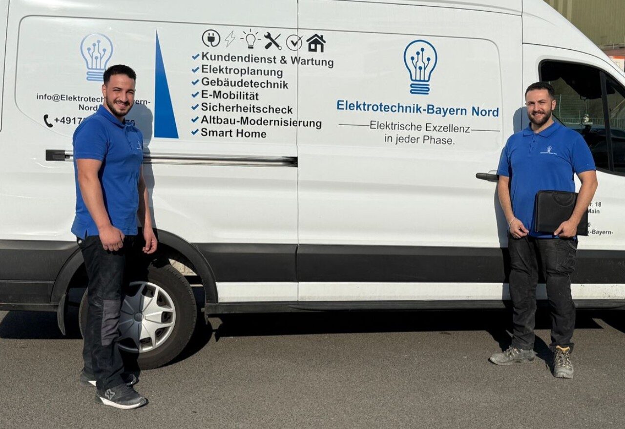 Zwei Mitarbeiter in blauen Polos vor beschriftetem Firmen-Transporter