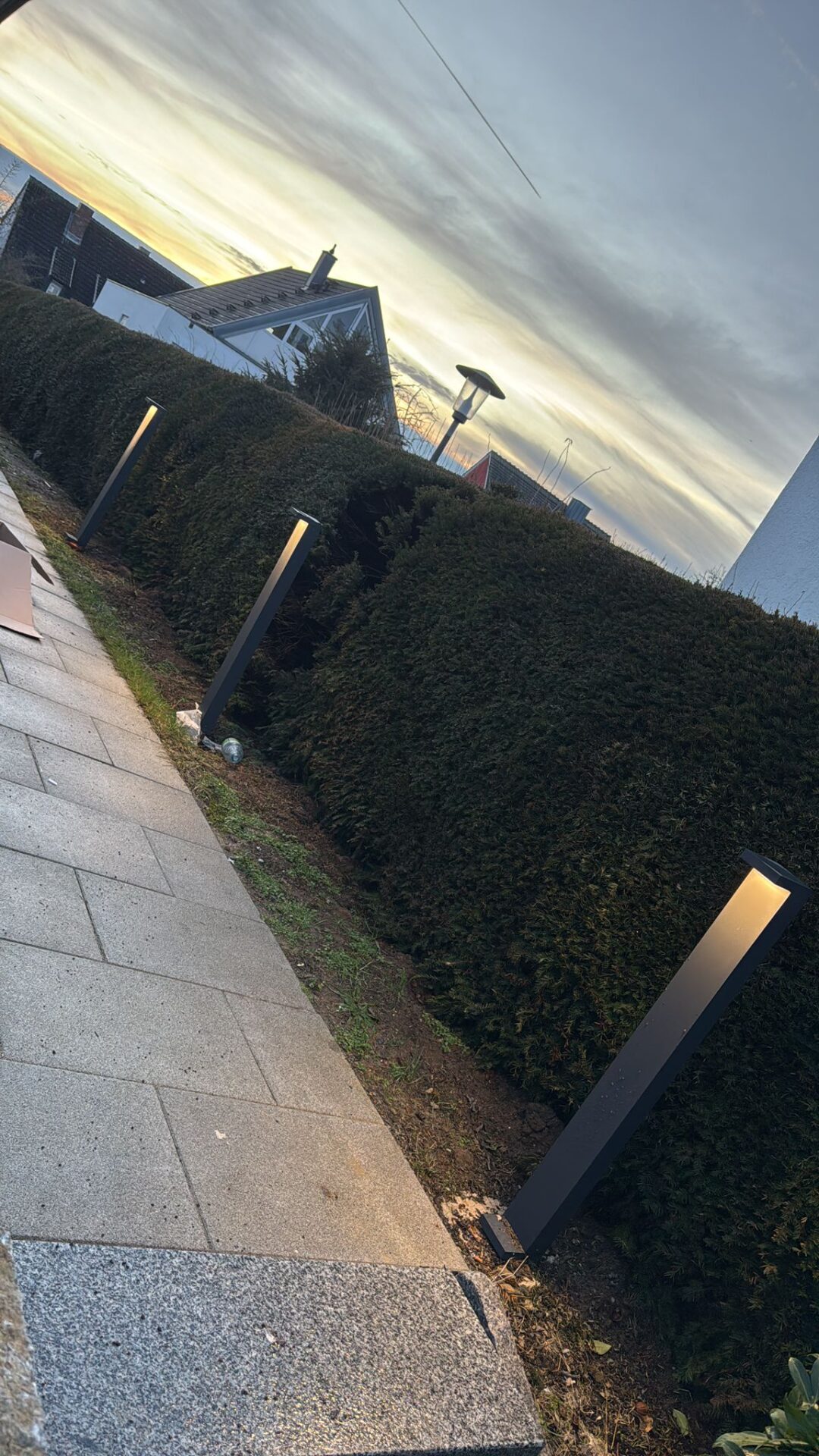 Anthrazitfarbene Wegeleuchten entlang eines Gehwegs an einer Hecke