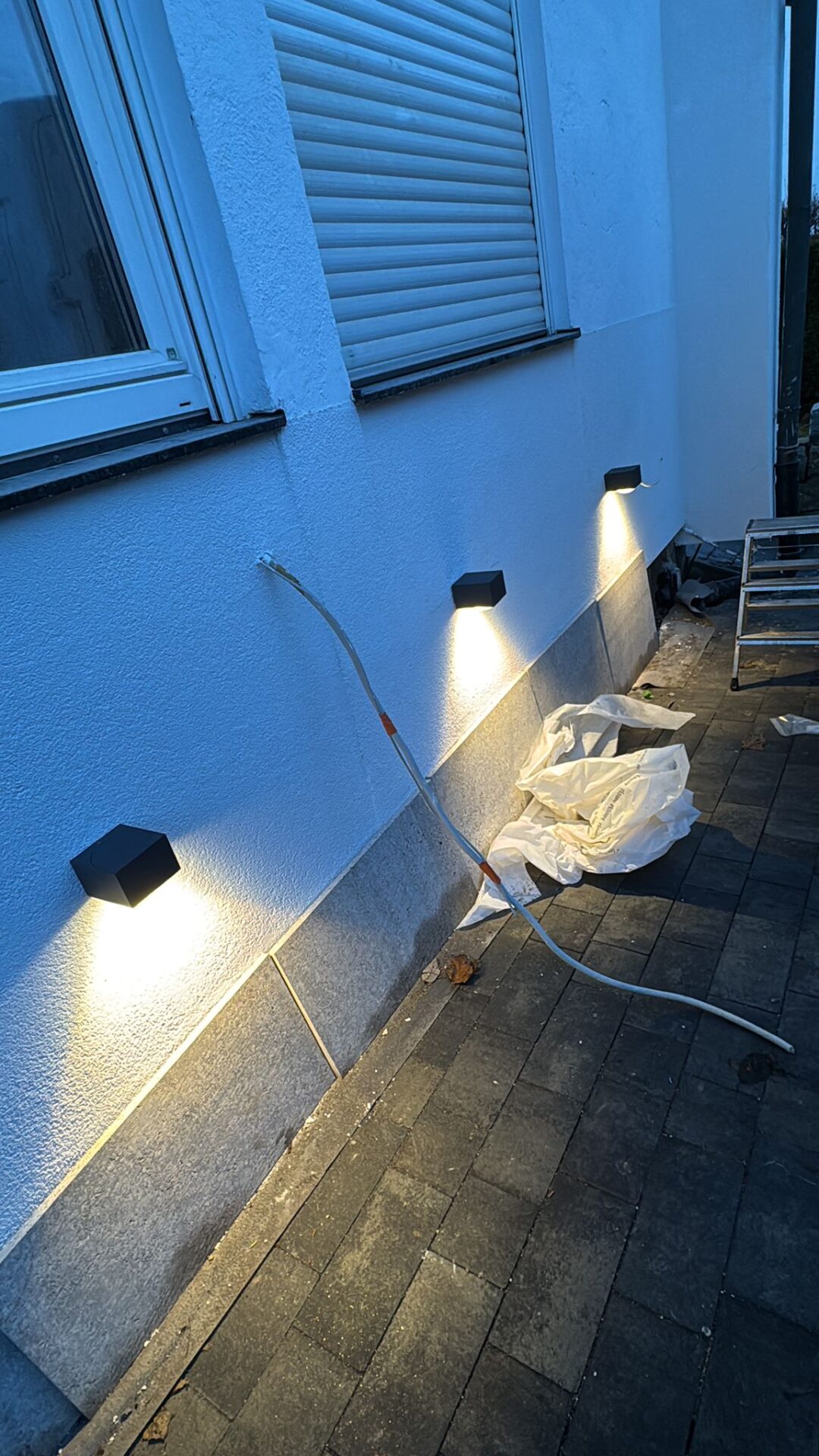 Beleuchtete schwarze Wandleuchten an einer Hausfassade in der Dämmerung