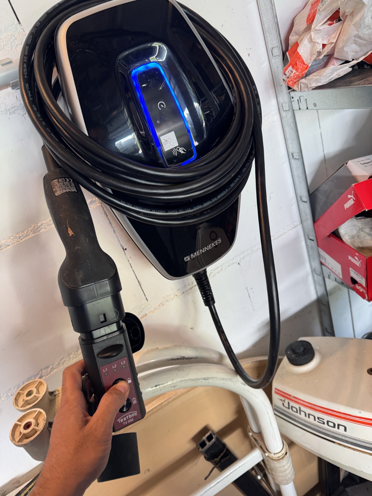 Elektriker prüft eine an der Garagenwand montierte Wallbox mit einem Spannungsprüfer