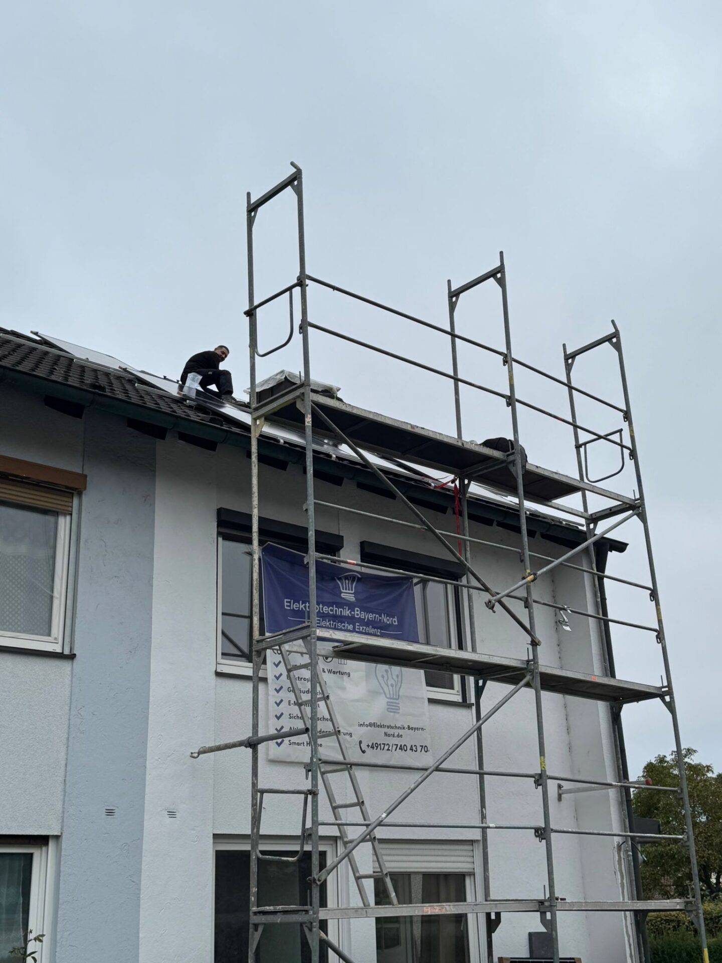 Monteur installiert Solarmodule auf Steildach hinter Gerüst