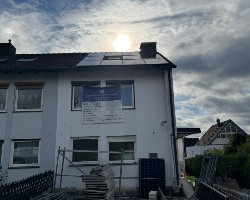 Haus mit Solarpanelen und Baumaterialien im Vordergrund.